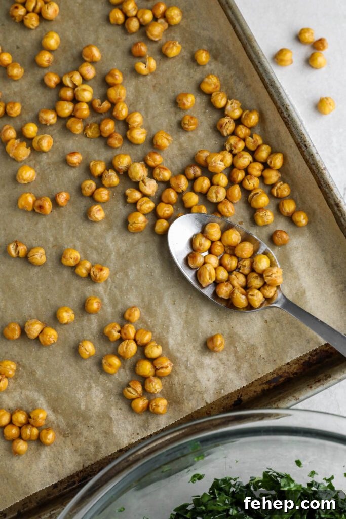 crispy chickpeas baked on parchment lined baking sheet with a spoon with a bowl of kale on the side