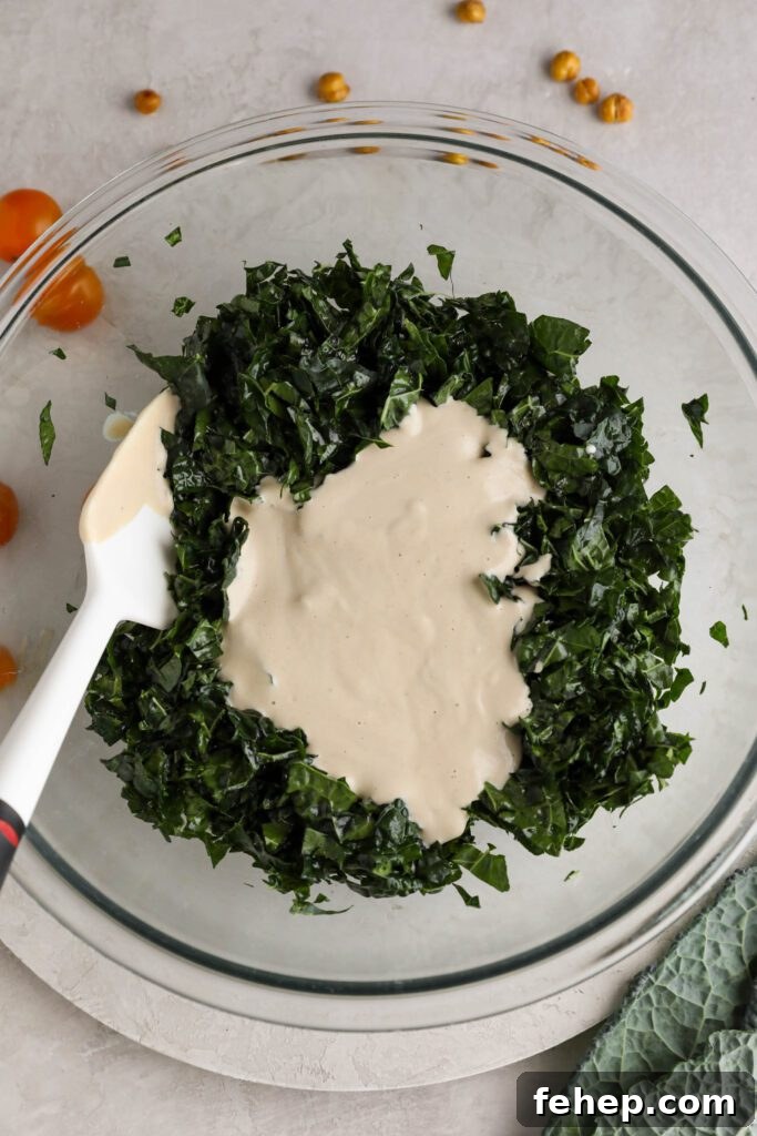 massaged kale in bowl with vegan caesar dressing poured on with spatula with cherry tomatoes and crispy chickpeas on the side