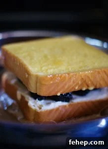 Two Texas-toast style slices of bread with fontina cheese and plump blackberries french toasting in a stainless steel skillet.