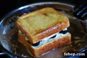Close up of French-toasted blackberry grilled cheese toasting in a stainless steel skillet. One side is golden brown.