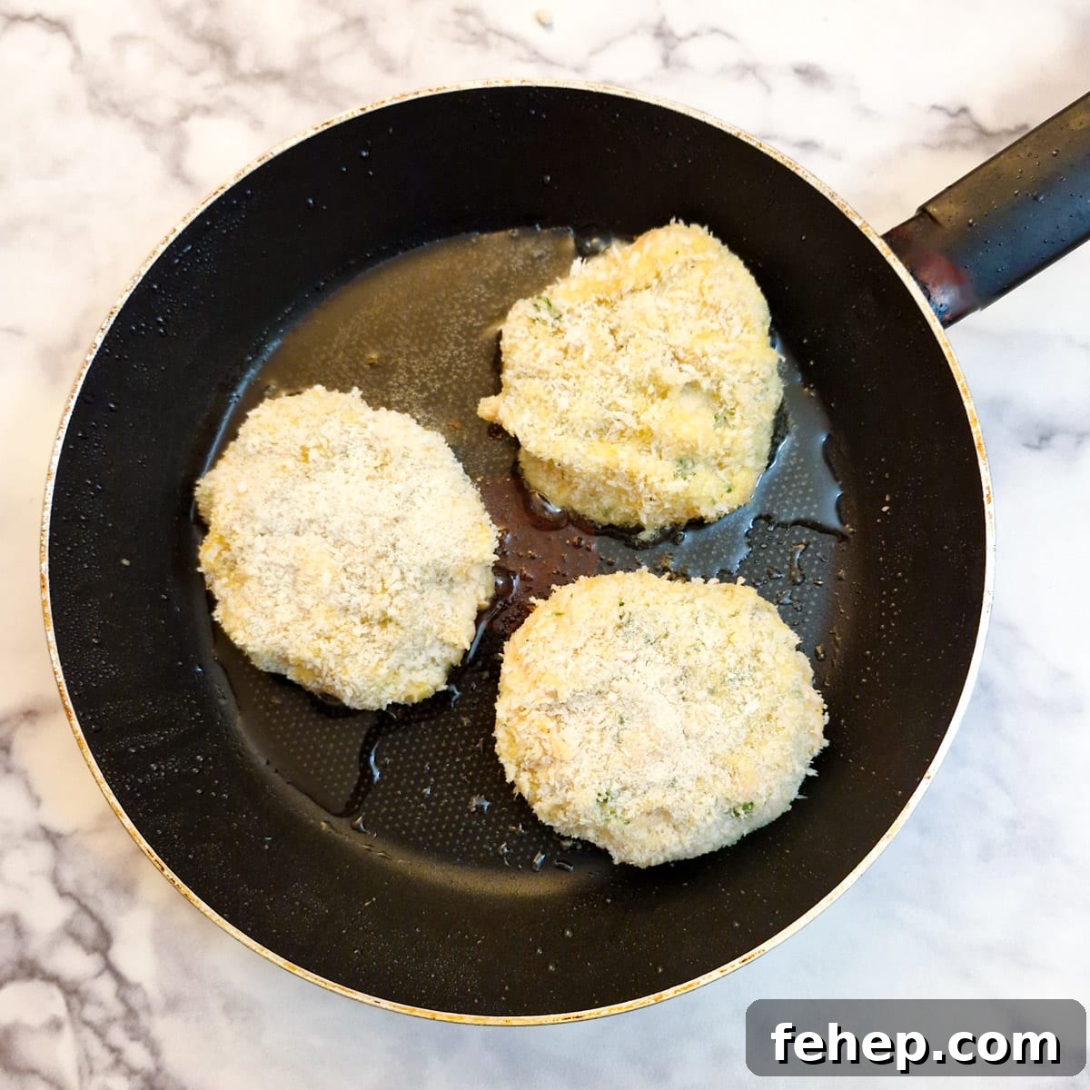 Crispy Salmon Fish Cakes with Lemon-Dill Sauce 14 3 salmon fishcakes in a frying pan.