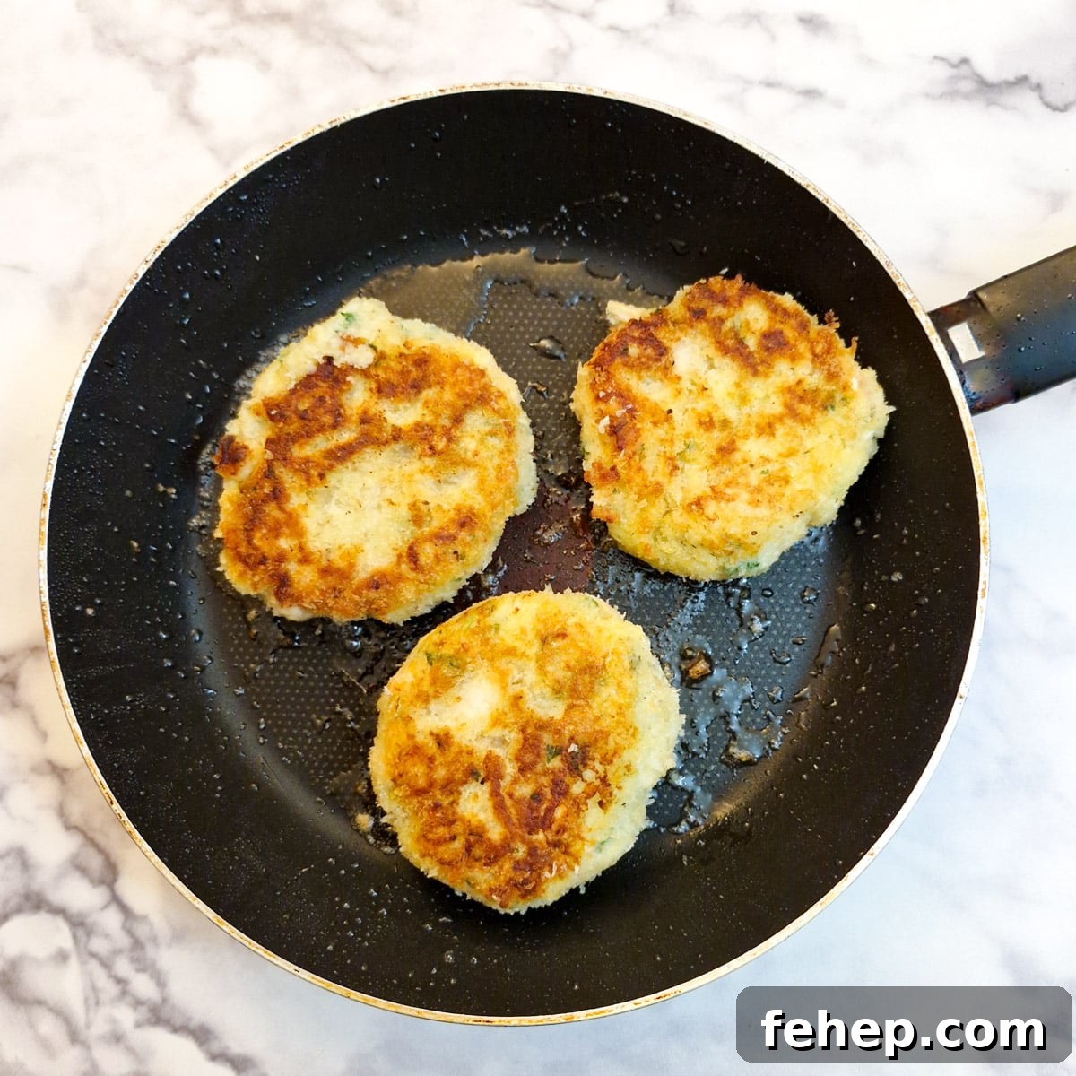 Crispy Salmon Fish Cakes with Lemon-Dill Sauce 15 3 browned salmon fishcakes in a frying pan.