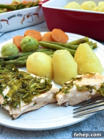 A piece of salmon covered in dill and parsley on a plate with potatoes and vegetables.