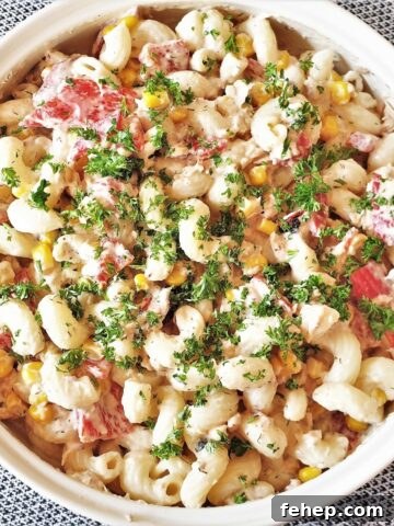 A bowl of salmon and red pepper pasta salad, sprinkled with chopped parsley.