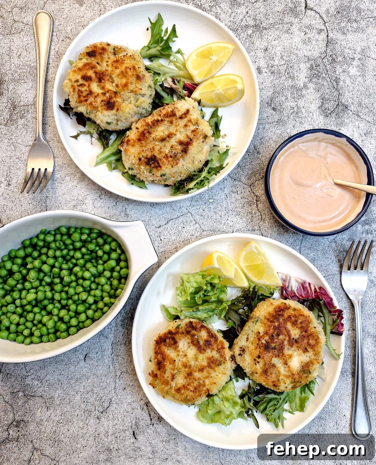 Crispy Salmon Fish Cakes with Lemon-Dill Sauce 3 Overhead shot of two plates of salmon fishcakes with a dish of peas and a dish of seafood sauce.