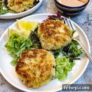 Crispy Salmon Fish Cakes with Lemon-Dill Sauce 21 Two salmon fishcakes on a white plate on a bed of lettuce with lemon slices.
