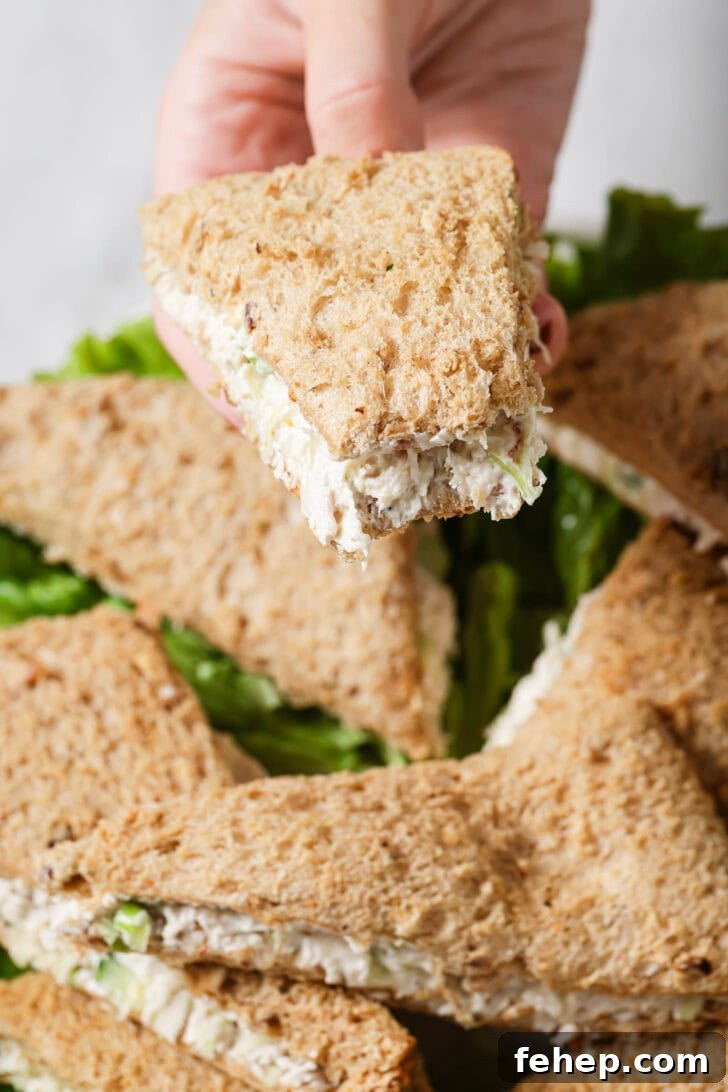 Creamy Chicken Mayo Sandwich Recipe for Balanced Flavor 18 Holding a partially eaten Chicken Sandwich over a platter of sandwiches.