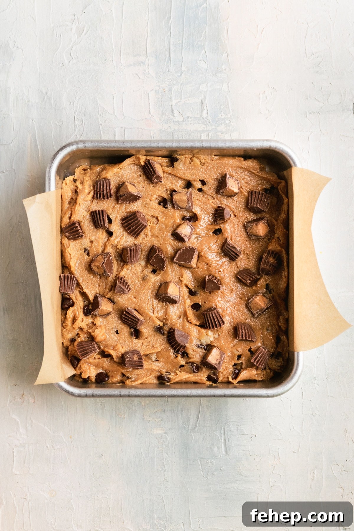 Chewy Peanut Butter Blondies Recipe with Melted Peanut Swirl 5 blondie batter in a square baking pan topped with Reese's peanut butter cups chopped into small pieces