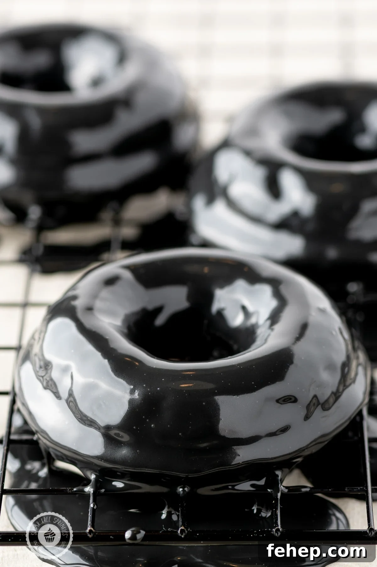 Keto Chocolate-Glazed Donuts for Halloween Treats 5 Black shiny ganache coated donuts on a cooling rack