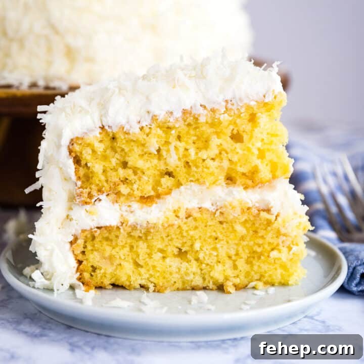 A slice of coconut cake on a place with the full cake behind it.