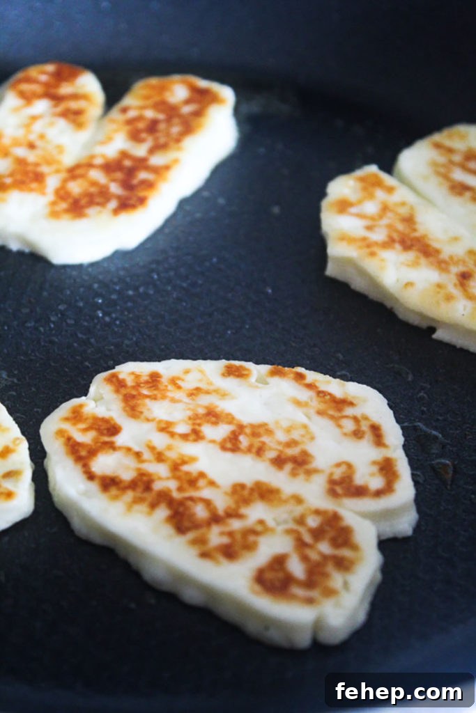 Lightly browned fried halloumi slices in a frying pan with olive oil.