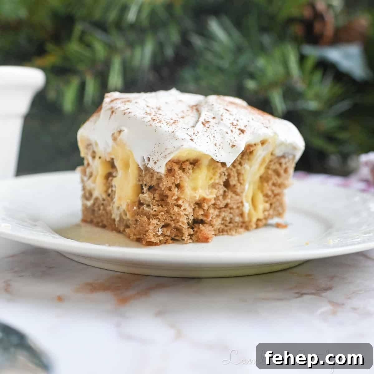 Creamy Eggnog Poke Cake Recipe for Holiday Gatherings 2 piece of eggnog poke cake on a plate in front of greenery and a baking pan.