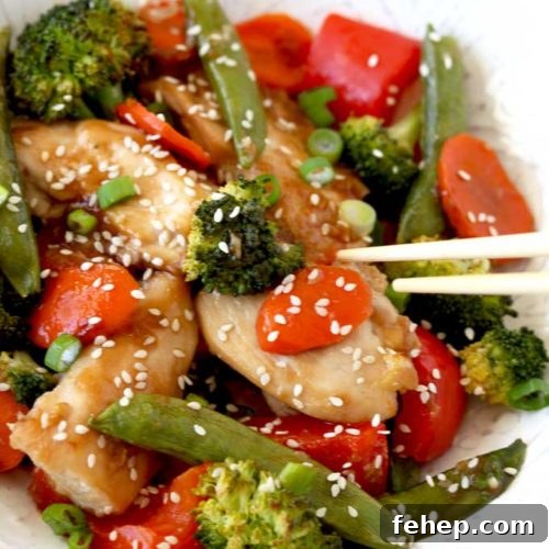 Sheet Pan Chicken and Vegetable Stir-Fry Recipe for Quick Dinners 6 Pictured here a white bowl filled with Asian Chicken and vegetables Stir Fry garnished with sesame seeds and sliced green onions.