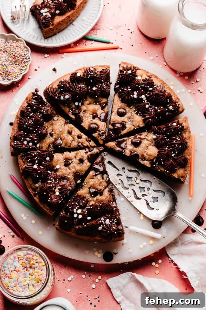 The sliced chocolate chip cookie cake on a marble plate, set on a pink backdrop. There are sprinkles and colorful birthday candles scattered around.