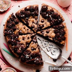 A photo of the sliced chocolate chip cookie cake on a marble plate. It's decorated with chocolate fudge frosting and sprinkles.