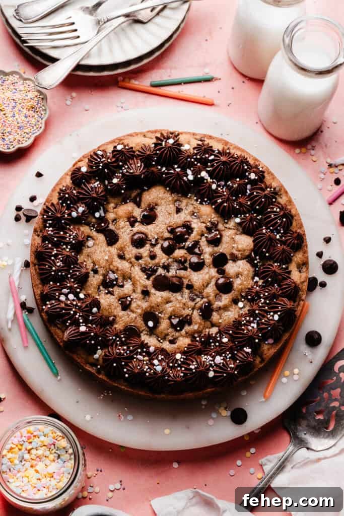 The baked chocolate chip cookie plate on a marble plate, decorated with chocolate fudge frosting and sprinkles.