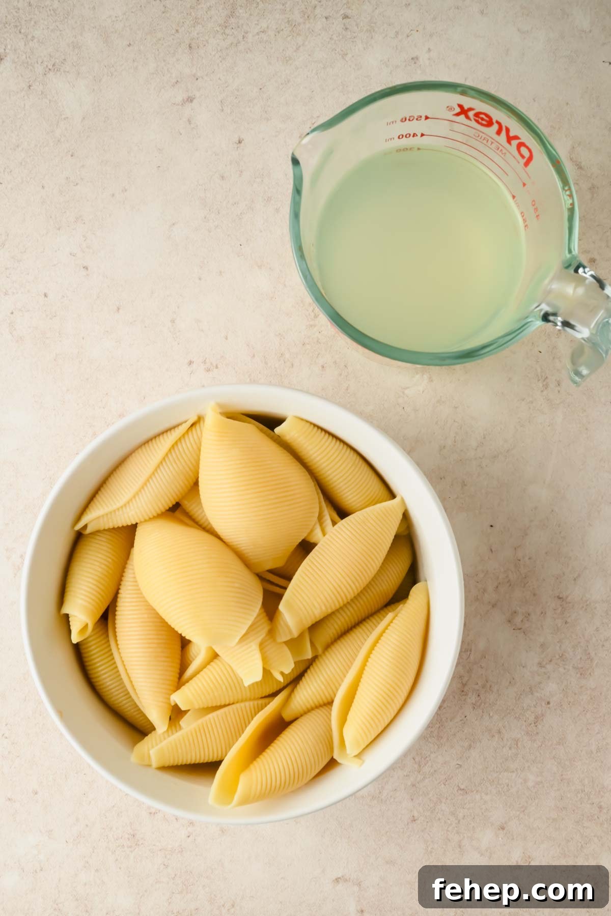 Unstuffed Shells Recipe: Cheesy Baked Pasta Skillet 4 cooked shell noodles in white bowl beside measuring cup of pasta water.