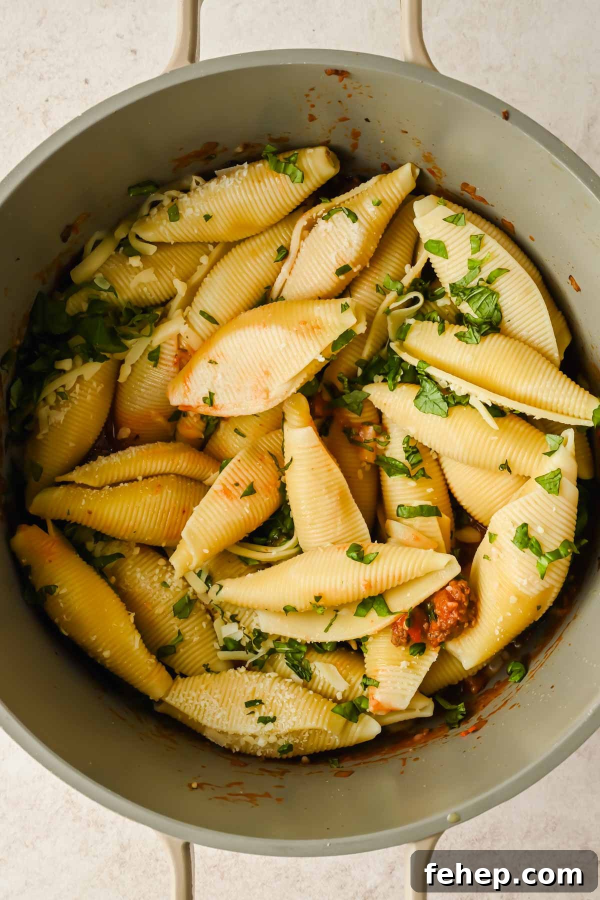 Unstuffed Shells Recipe: Cheesy Baked Pasta Skillet 7 shell pasta noodles topped with chopped basil in a red meat sauce in a large pot.
