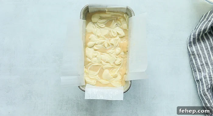 A picture of dollops of cream cheese swirls on top of banana bread batter in a loaf pan 