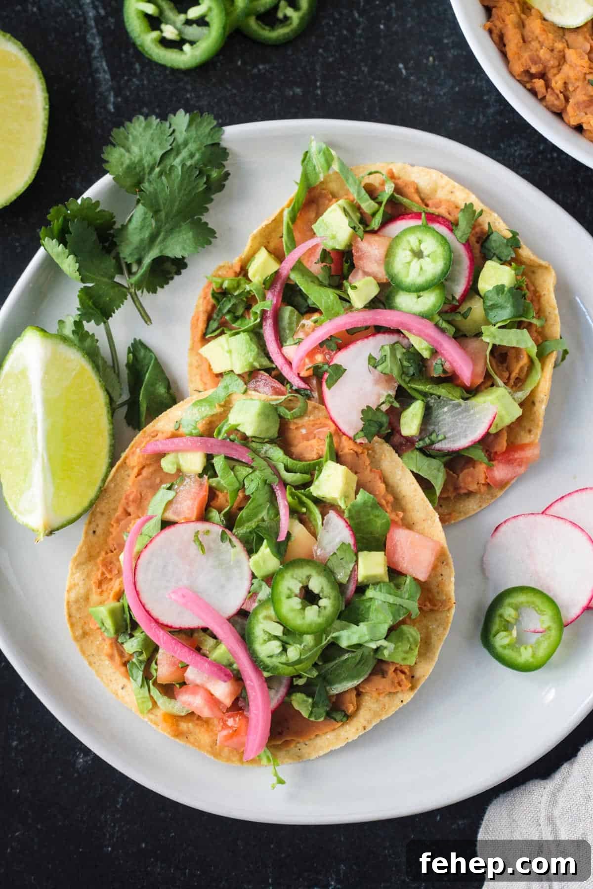 Two crispy baked flat tortillas with lots of toppings next to a lime wedge.