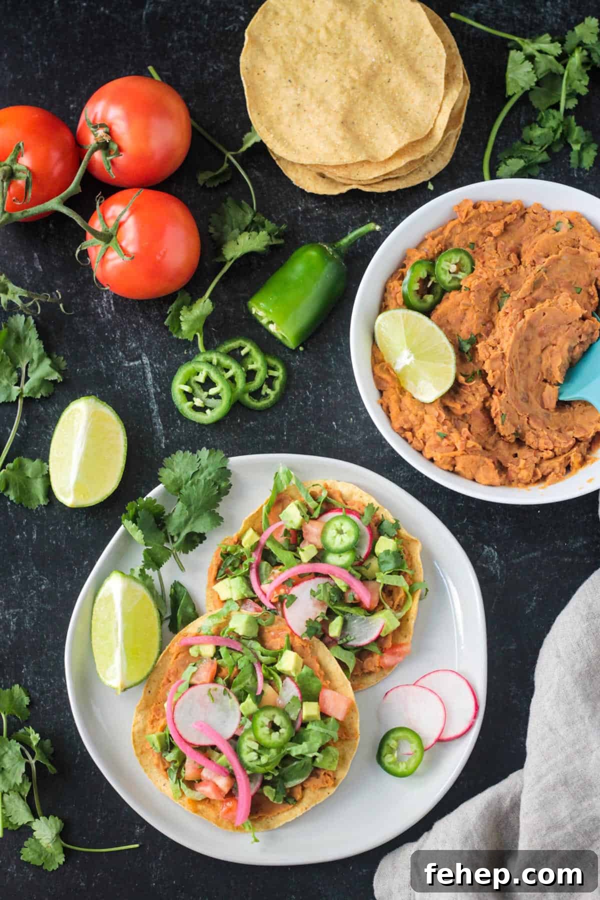 Two vegan tostadas on a plate next to a bowl of refried benas.