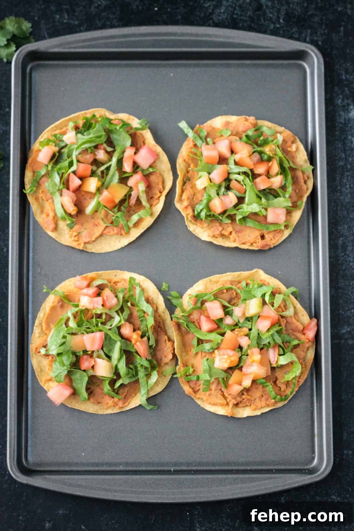 4 crispy corn tortillas topped with beans, lettuce, and tomato.