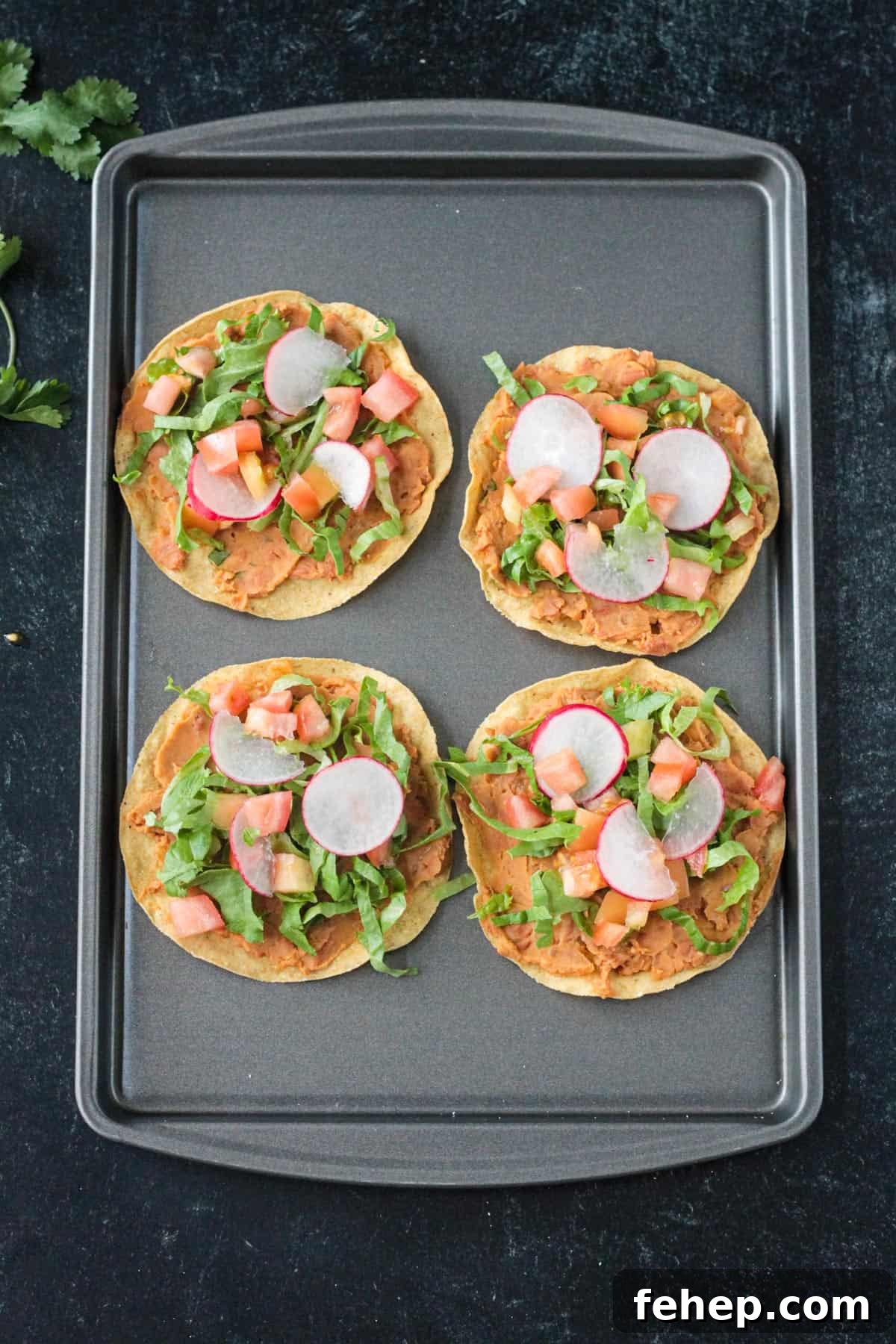 4 crispy corn tortillas topped with beans, lettuce, tomato, avocado, and radishes.