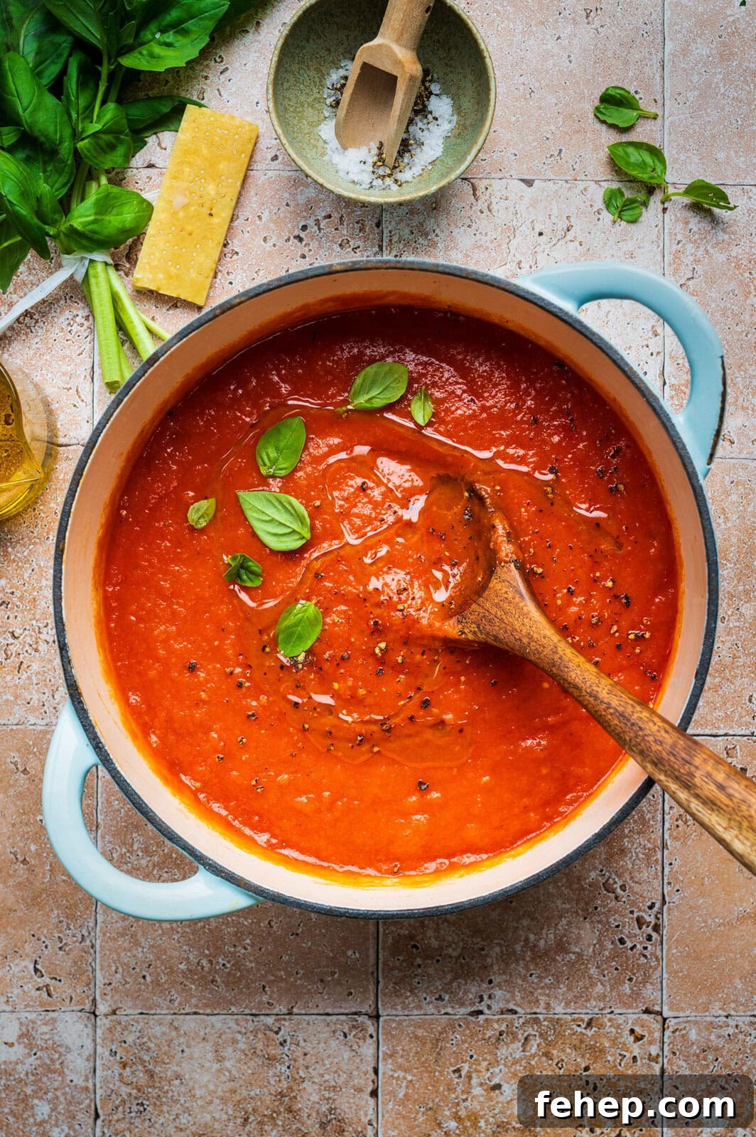 Authentic San Marzano Tomato Sauce Recipe for Rich Flavor 2 A pot of San Marzano tomato sauce garnished with basil leaves sits on a tiled surface. A wooden spoon rests inside the pot. Fresh basil, a wedge of cheese, salt, and olive oil are arranged nearby.