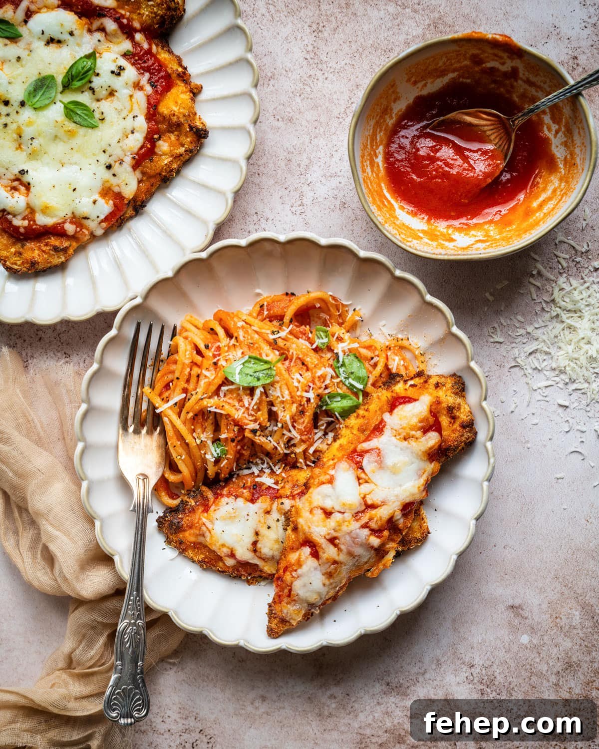 Authentic San Marzano Tomato Sauce Recipe for Rich Flavor 8 A plate with spaghetti topped with tomato sauce and grated cheese, served alongside chicken parmesan with melted cheese. Another plate with chicken parmesan and a small bowl of tomato sauce are nearby.