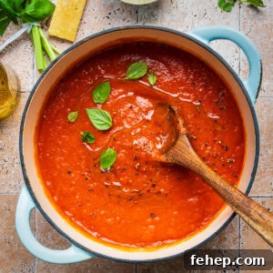 Authentic San Marzano Tomato Sauce Recipe for Rich Flavor 9 A pot of San Marzano tomato sauce garnished with basil leaves sits on a tiled surface. A wooden spoon rests inside the pot. Fresh basil, a wedge of cheese, salt, and olive oil are arranged nearby.
