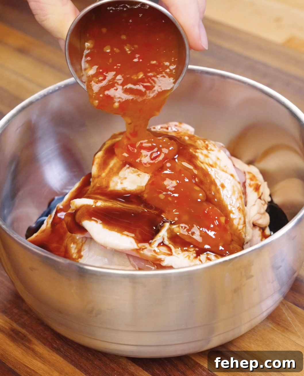 Sweet chili sauce being poured over raw chicken thighs in a bowl with soy sauce and oyster sauce marinade.