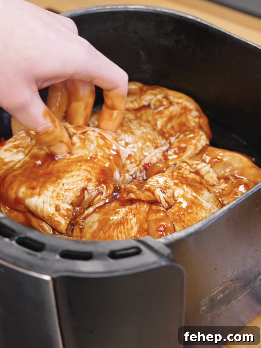 Hand arranging marinated chicken thighs inside an air fryer basket before cooking.