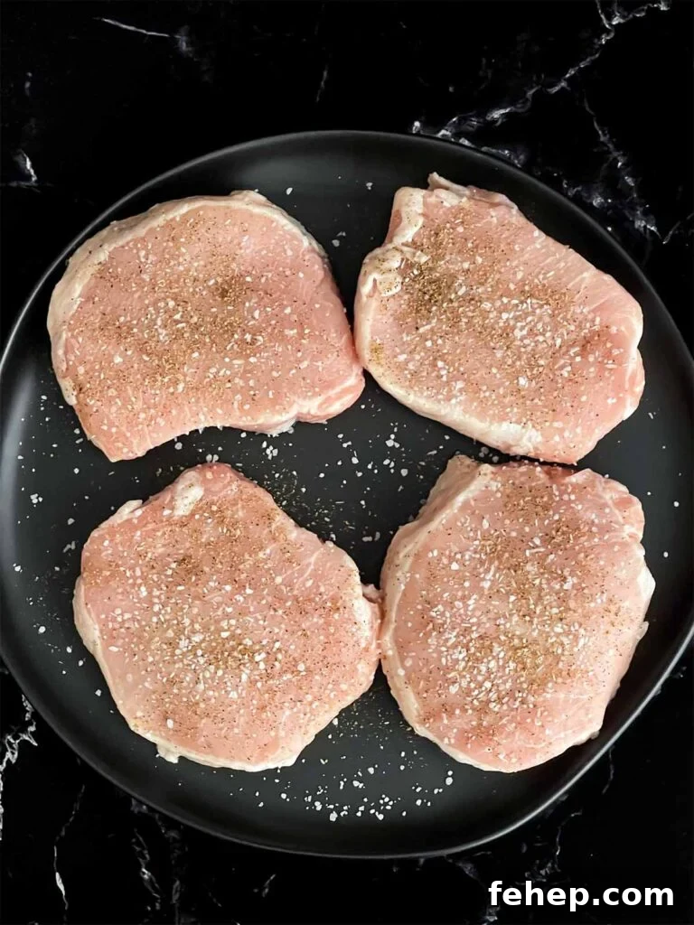 Spanish-Style Pork Chops with Garlic Tomato Rice 3 Boneless pork chops seasoned with kosher salt and black pepper on a dark plate.