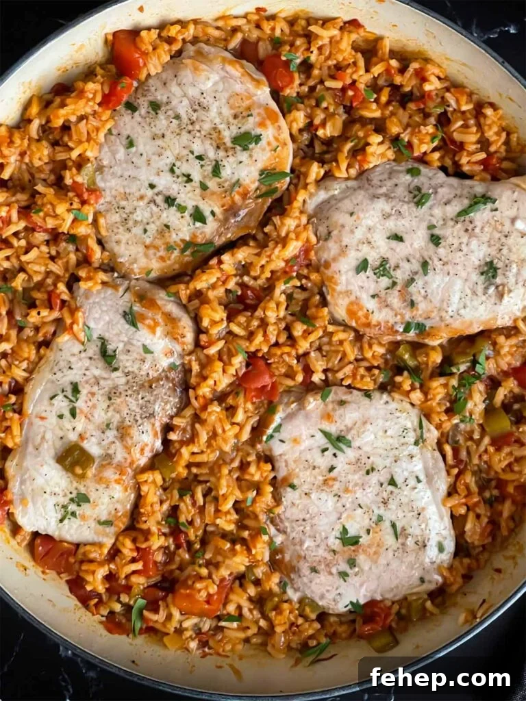 Spanish-Style Pork Chops with Garlic Tomato Rice 8 Spanish pork chops and rice garnished with chopped parsley in a light colored skillet.