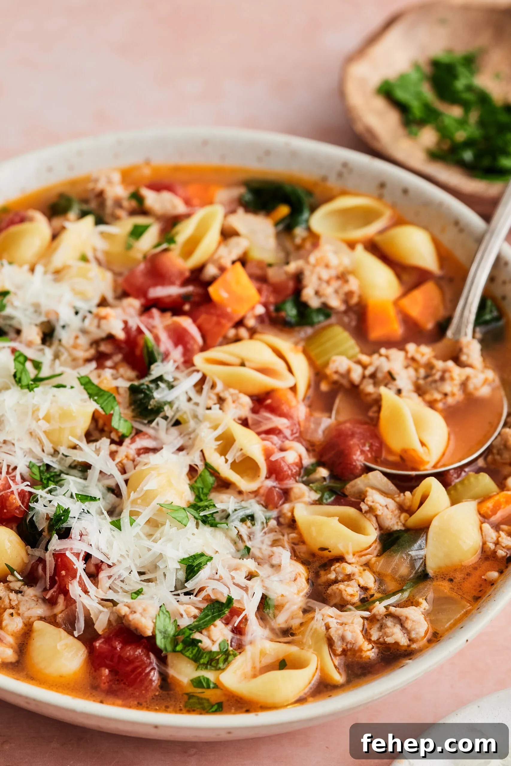 25 Comforting Fall Dinner Ideas for Cozy Weeknight Meals 2 Bowl of Italian sausage soup topped with cheese and fresh herbs, with a spoon scooping out a serving against a light pink background.