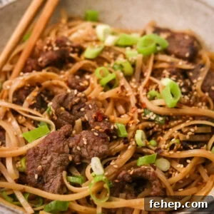 Bowl of Mongolian beef and noodles with green onions and sesame seeds on top
