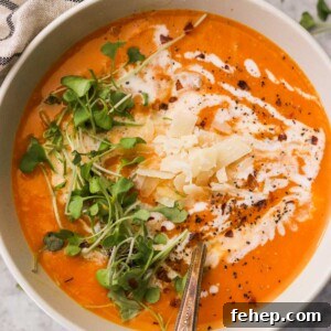 a closeup of creamy butternut squash soup with coconut milk topped with parmesan cheese, microgreens, and black pepper