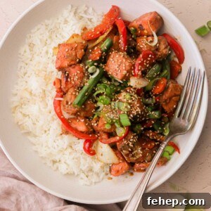 an overhead view of a white plate filled with white rice and salmon stir fry with a silver fork resting on the side of the plate
