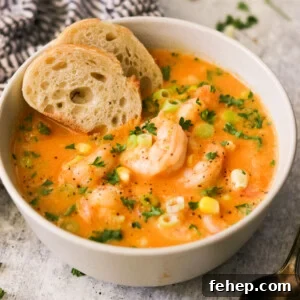 side view of a bowl of soup topped with garnishes and shrimp and two slices of bread.