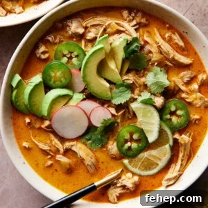A bowl of keto white chicken chili with shredded chicken, avocado slices, jalapeños, cilantro, radish, and lime.