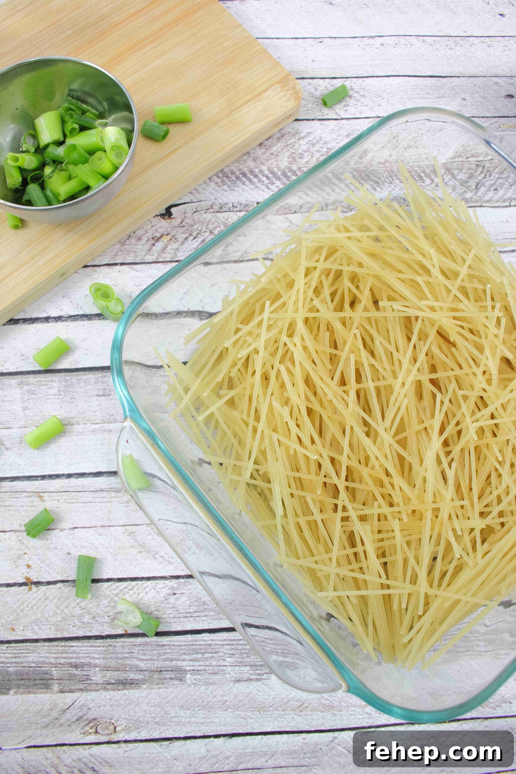 Gluten-Free Dairy-Free Chicken Alfredo Casserole Recipe 4 Raw noodles in a clear casserole dish with green onions beside it.