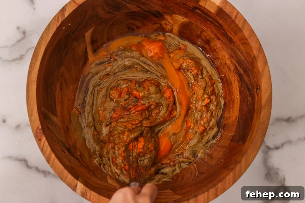 Large wooden bowl with almond butter, sweet potato puree, maple syrup, egg, and vanilla extract.
