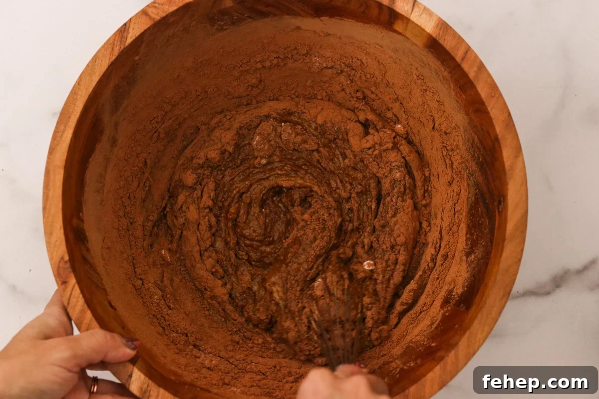 Cocoa powder, baking soda, and sea salt being stirred into the same wooden bowl.