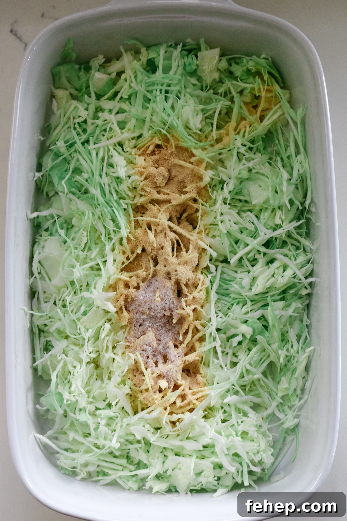 shredded cabbage in a white baking dish with seasonings on top.