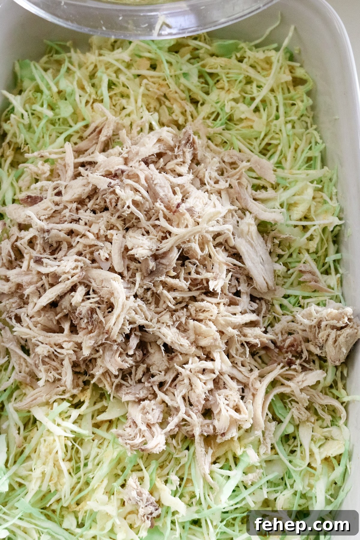 shredded cabbage and shredded chicken in a white baking pan.