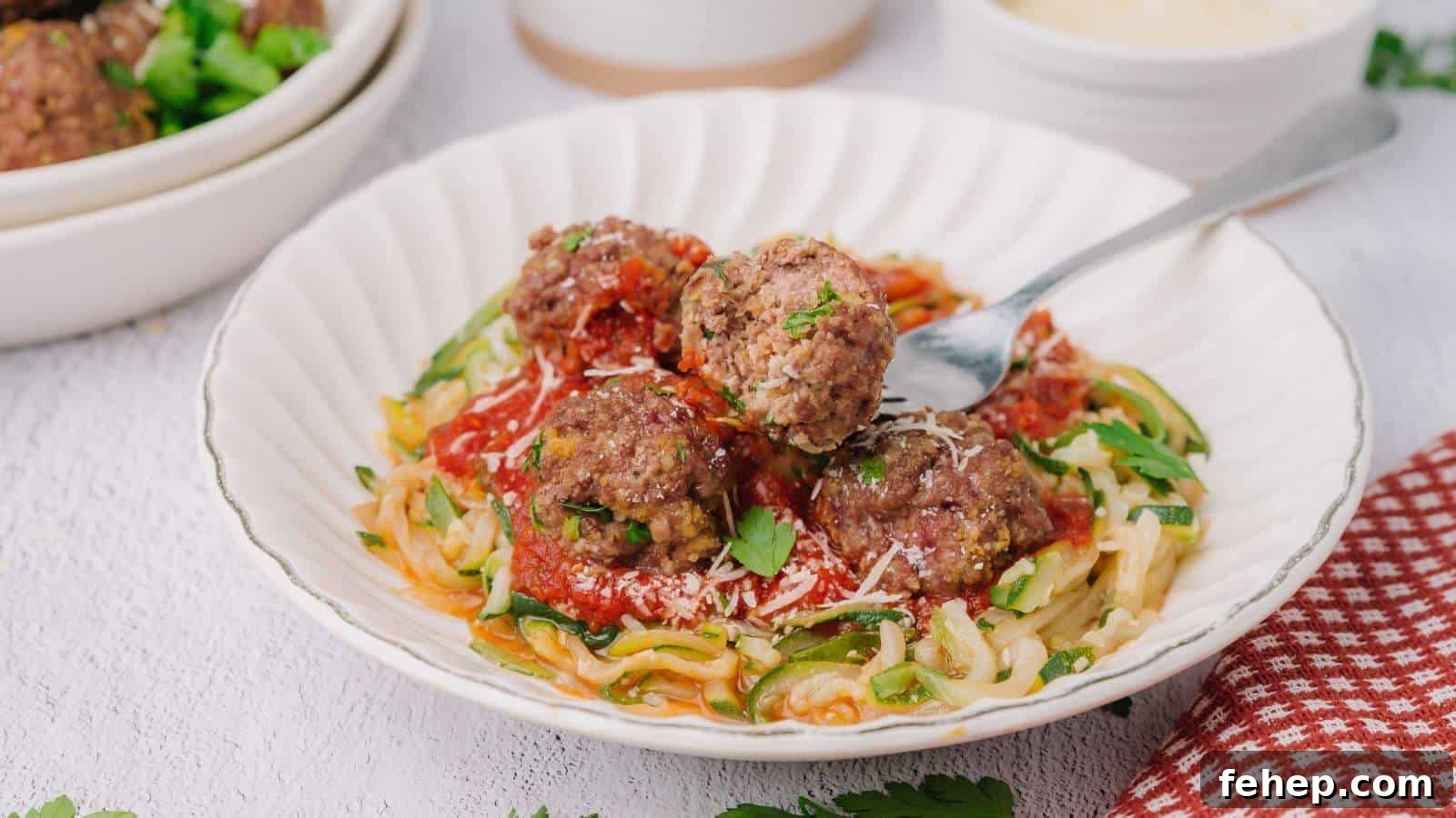 19 Authentic Italian Dinners That Feel Effortless and Homey 14 A plate of zucchini noodles topped with tomato sauce, meatballs, and grated cheese, garnished with parsley. A fork rests on the plate.