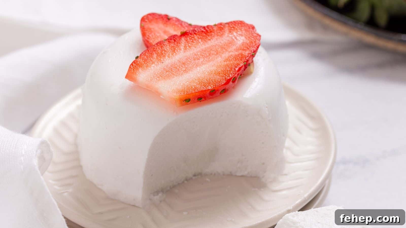 19 Authentic Italian Dinners That Feel Effortless and Homey 8 A slice of white, creamy panna cotta topped with a fresh strawberry slice on a white plate, with a textured napkin beside it.