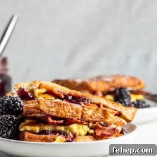 Bacon and Blackberry French Toast Sandwich Recipe 3 French toast sandwich on a white plate with gray background and second plate in the background.