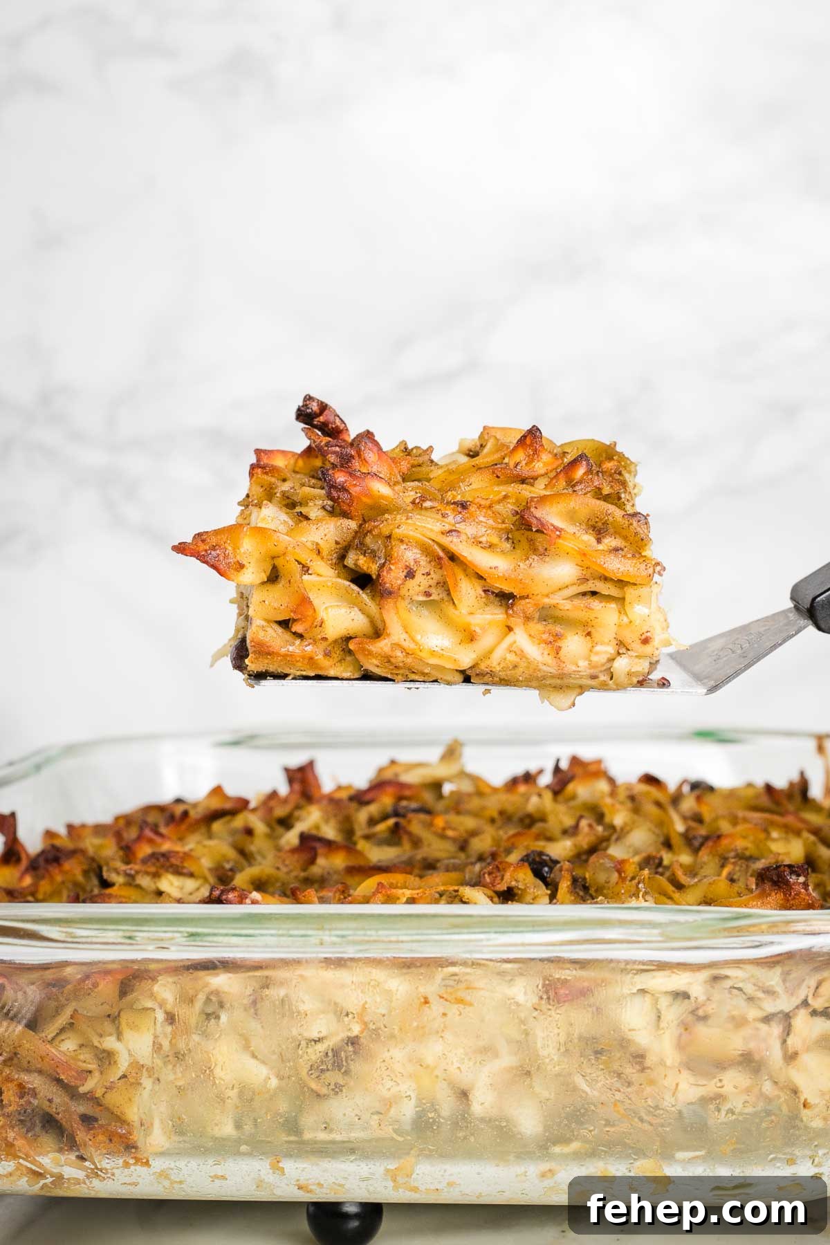 Piece of noodle kugel pulled up on a spatula above the entire casserole.