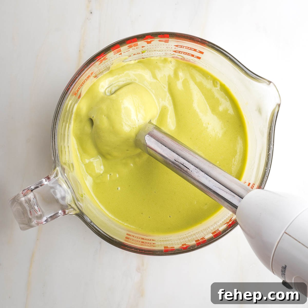 Immersion blender in a large measuring cup with a light green colored creamy mixture.
